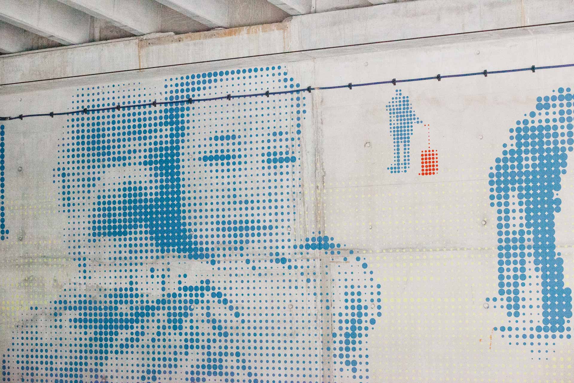 kunstwerk op wand opgebouwd uit blauwe stippen, twee vrouwen omhelzen elkaar